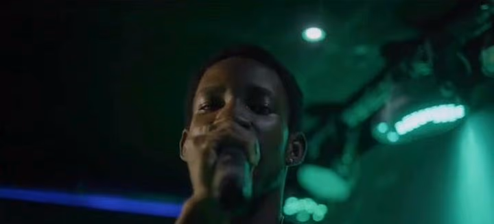A performer raps into a microphone, lit by green stage lights