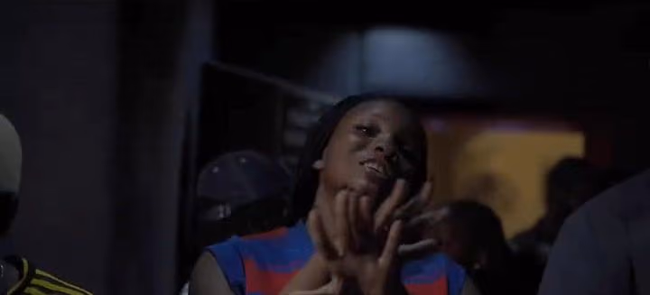 A woman in a red and blue jersey dances with her hands together