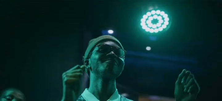 A dancer in a bucket hat raises his hands under a teal stage light at the Afro Frequency night
