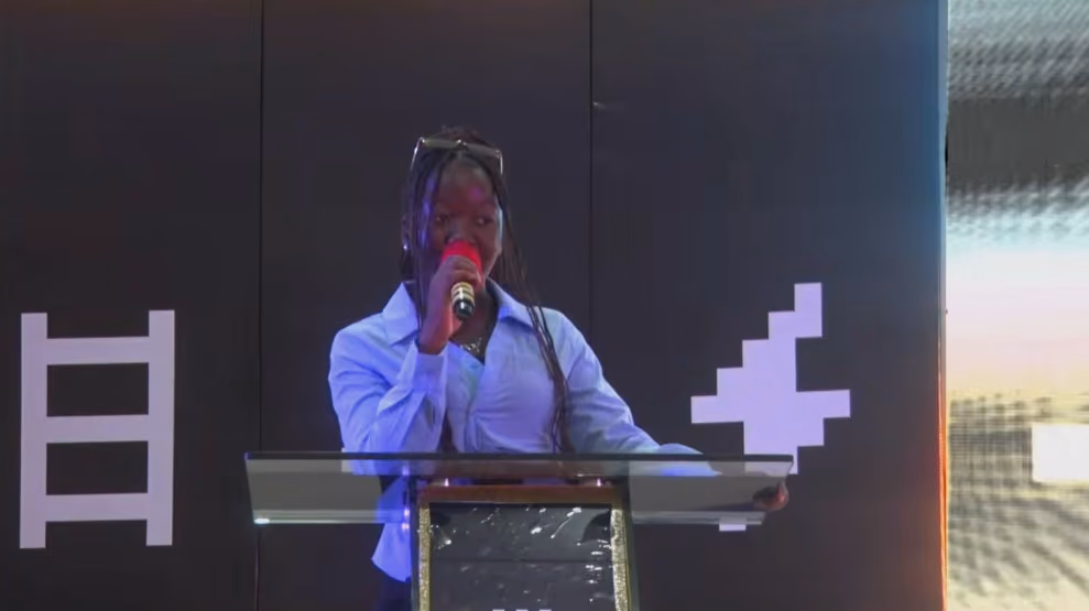 A student speaks into a microphone at a glass lectern on the AWS Student Community Day stage