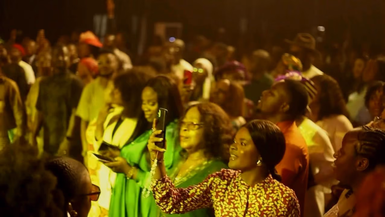 Guests in bright outfits film the service on their phones from the crowd