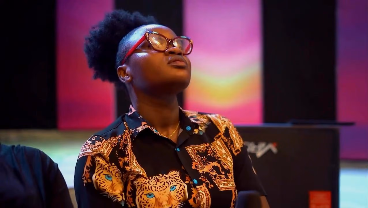 A worshipper in glasses looks up in front of glowing pink and purple stage panels at Worship Realm