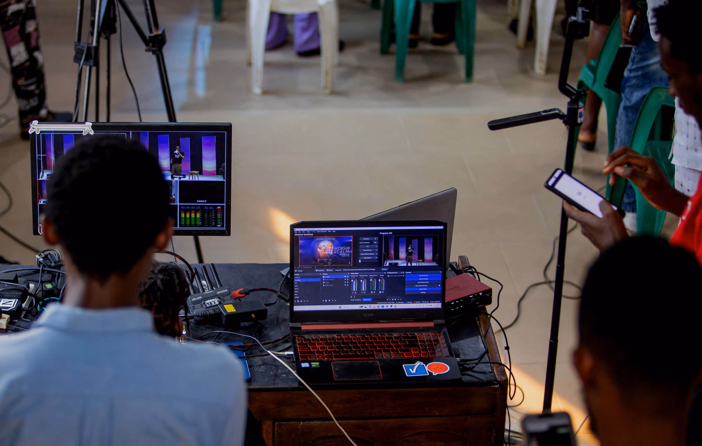 Production desk with a switcher laptop and monitor seen over the shoulder of a seated viewer