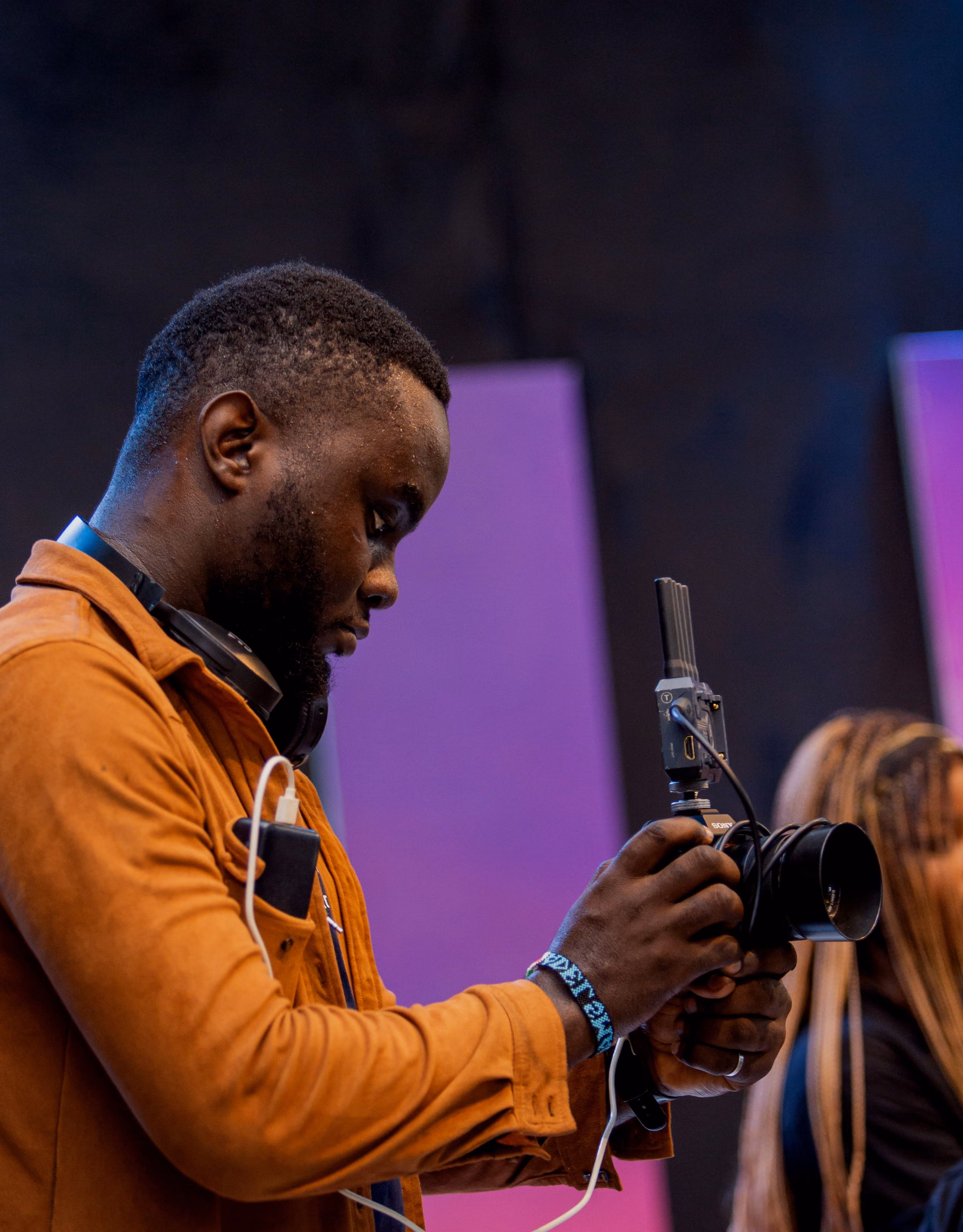 Operator in a mustard jacket checking a handheld gimbal camera against a purple stage backdrop